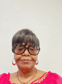 an older woman wearing glasses and a pink top smiles for the camera