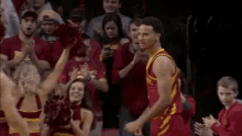 a basketball player in a red jersey with the word state on it is standing in front of a crowd of cheerleaders .