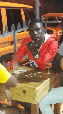 a man in a red jacket sits at a wooden table