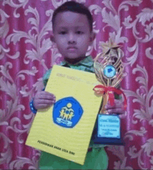 a young boy is holding a trophy and a certificate that says pendidikan anak usia dini