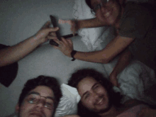 three men are laying on a bed and one is holding a tablet