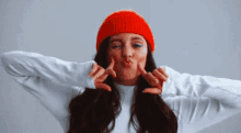 a woman wearing a red beanie and a white sweater is making a funny face