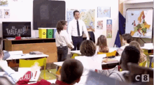 a man in a suit and tie stands in front of a group of children in a classroom with a sign that says au tableau