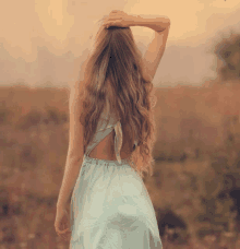 a woman in a blue dress is standing in a field holding her hair