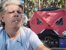 a man smoking a cigarette with a tent in the background