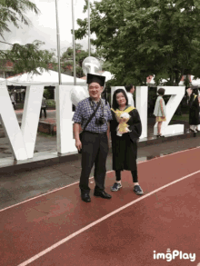 a woman in a graduation cap and gown poses with a man in front of a sign that says viz