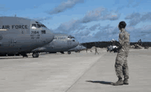 a woman in a military uniform is standing on a runway in front of a row of airplanes .