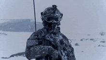 a soldier in a helmet and goggles is standing in the snow holding a rifle .