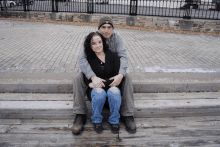 a man and a woman pose for a picture on a wooden bench