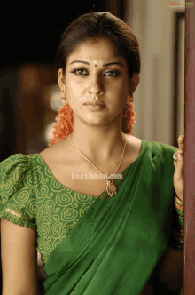 a woman wearing a green saree and a green blouse is standing in front of a sign that says ragalahari