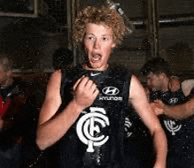 a young man with curly hair is standing in front of a group of people in a room .