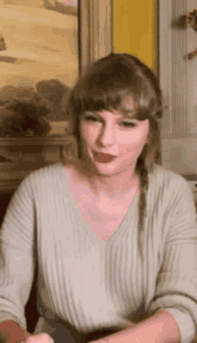 taylor swift is wearing a sweater and red lipstick while sitting in front of a painting .