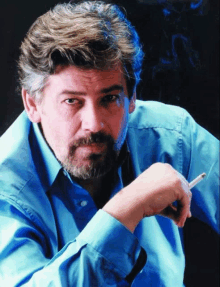 a man with a beard is smoking a cigarette and wearing a blue shirt