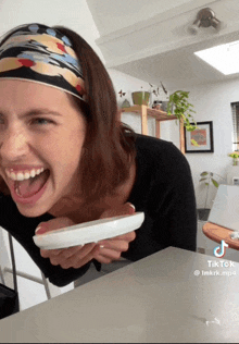 a woman wearing a headband is laughing and holding a white plate in her hands