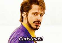 a man with a beard is wearing a purple suit and yellow shirt and says christmas