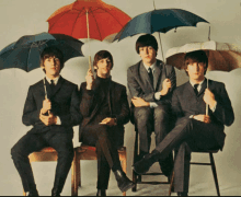 four men sitting on stools holding umbrellas