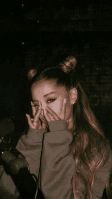 ariana grande covering her face with her hands in front of a microphone