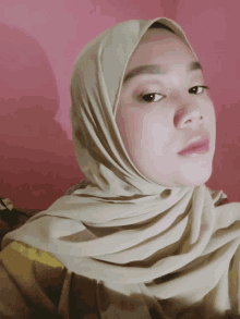 a woman wearing a beige hijab looks at the camera