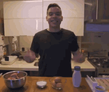 a man in a black shirt is standing in a kitchen with a bowl of eggs and a bottle of mayonnaise