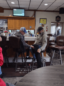 two men sit at a bar in front of a sign that says ' steak golf '