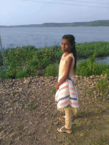 a little girl in a striped dress stands in front of a large body of water