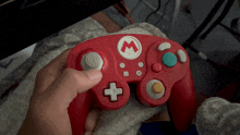 a person holding a red game controller with a white m on it