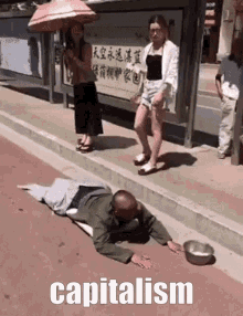 a man is laying on the side of the road with a bowl of food and the word capitalism above him .