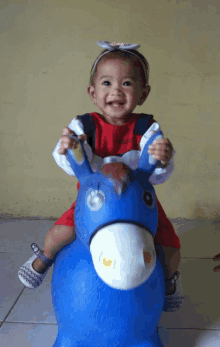 a little girl wearing a red shirt that says ' adidas ' on it sits on a blue toy donkey