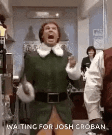 a man in a green elf costume is screaming in a room while waiting for josh groban .