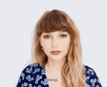 taylor swift is wearing a blue and white floral shirt and talking to the camera while standing in front of a white background .