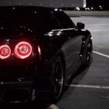 a black car with red lights is parked in a parking lot at night