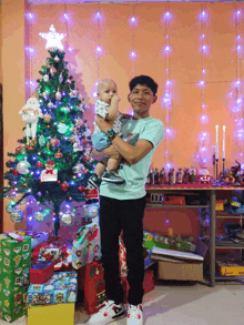 a man holding a baby in front of a christmas tree with a star on top