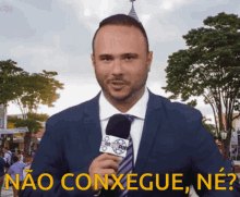 a man in a suit and tie holds a microphone in front of a sign that says " não consegue ne "