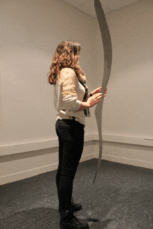 a woman in a white sweater and black jeans stands in a room