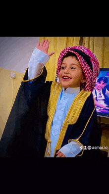 a young boy wearing a turban and a coat is smiling and waving his hand