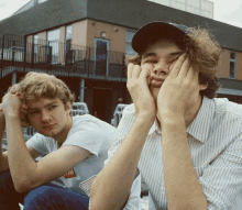 two young men are sitting in front of a building with one wearing a shirt that says " supreme "