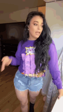 a woman is wearing a purple sweater and denim shorts .