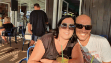 a man and a woman are posing for a picture while sitting at a table with a drink in front of them