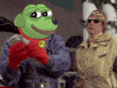 a man wearing sunglasses is standing next to a green frog