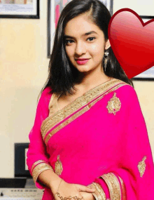 a woman in a pink saree is standing in front of a red heart