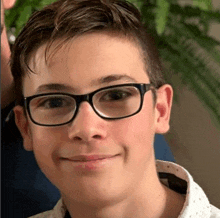 a young man wearing glasses and a white shirt is smiling .