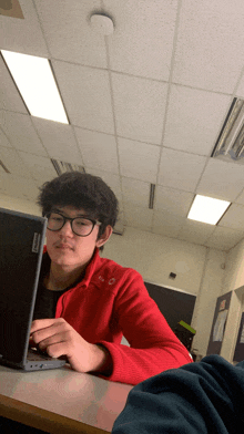 a young man in a red jacket is using a lenovo laptop computer