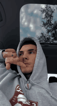 a man wearing a grey hoodie with the letter g on it is sitting in a car