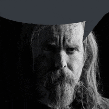 a man with long hair and a beard is wearing a cowboy hat in a black and white photo .