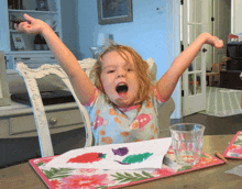 a little girl sits at a table with her arms outstretched