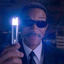 a man wearing sunglasses and a suit is holding a light bulb in his hand .