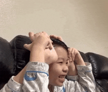 a young boy is sitting on a couch with his hands on his head and making a face .