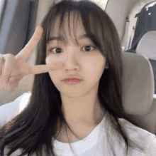 a young woman is sitting in a car making a peace sign with her hand .