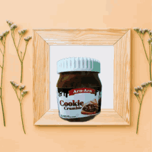 a jar of cookie crumble sits in a wooden frame surrounded by flowers