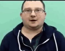 a man wearing glasses and a black hoodie is talking to the camera .